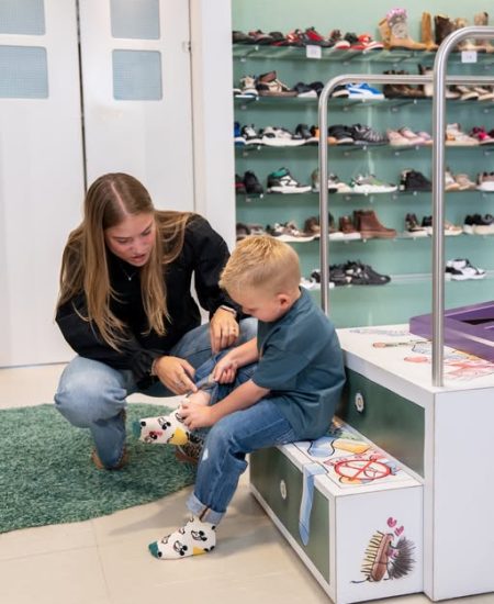 Een medewerker helpt een kind met het passen van Lightvoet-schoenen in de winkel.